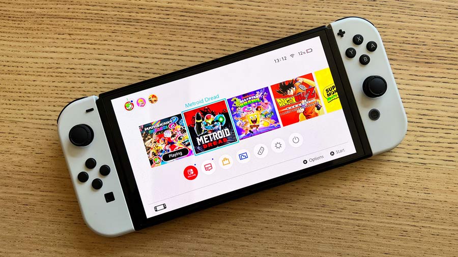 تصویر کنسول نینتندو سوییچ مدل OLED با نمایش منوی بازیهایی مانند Metroid Dread، Mario Kart، Dragon Ball و Super Mario روی صفحه نمایش.